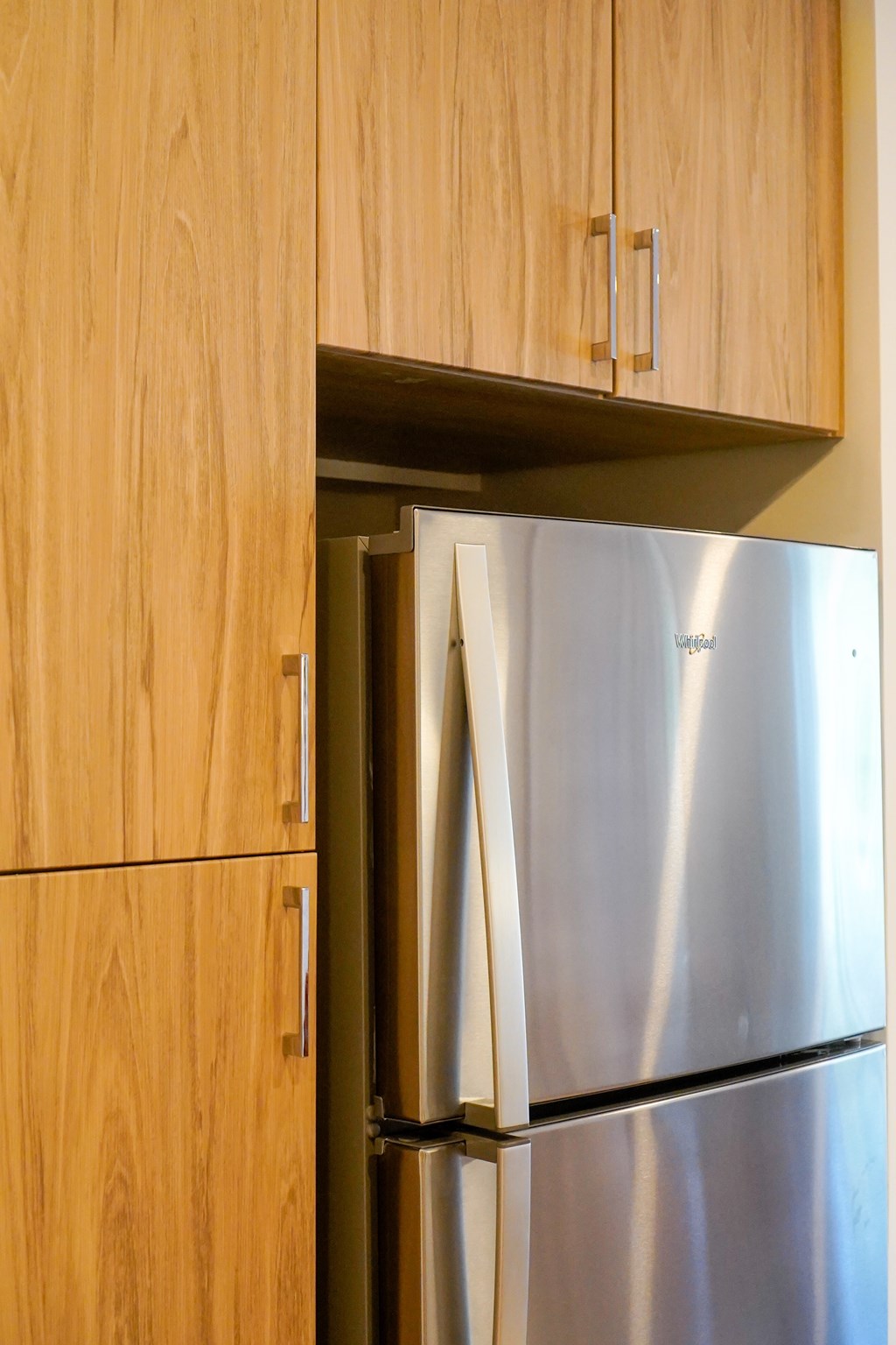 A stainless steel refrigerator is built into a wooden cabinet.