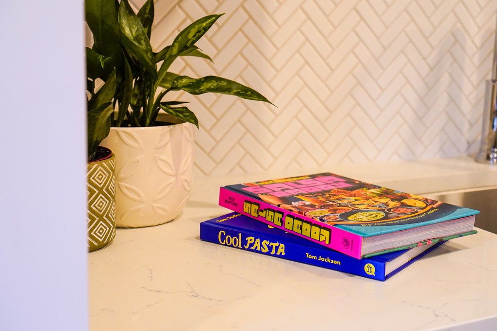 A stack of cookbooks titled "Cool Pasta" by Ten Jackson sits on a countertop.