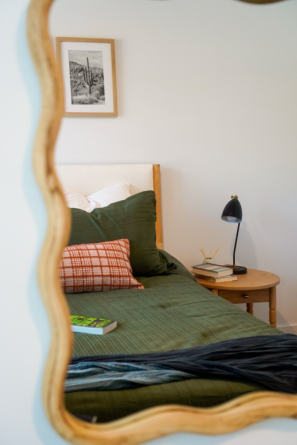 A bedroom with a bed, a small table with a lamp and a book on it, and a framed picture on the wall.