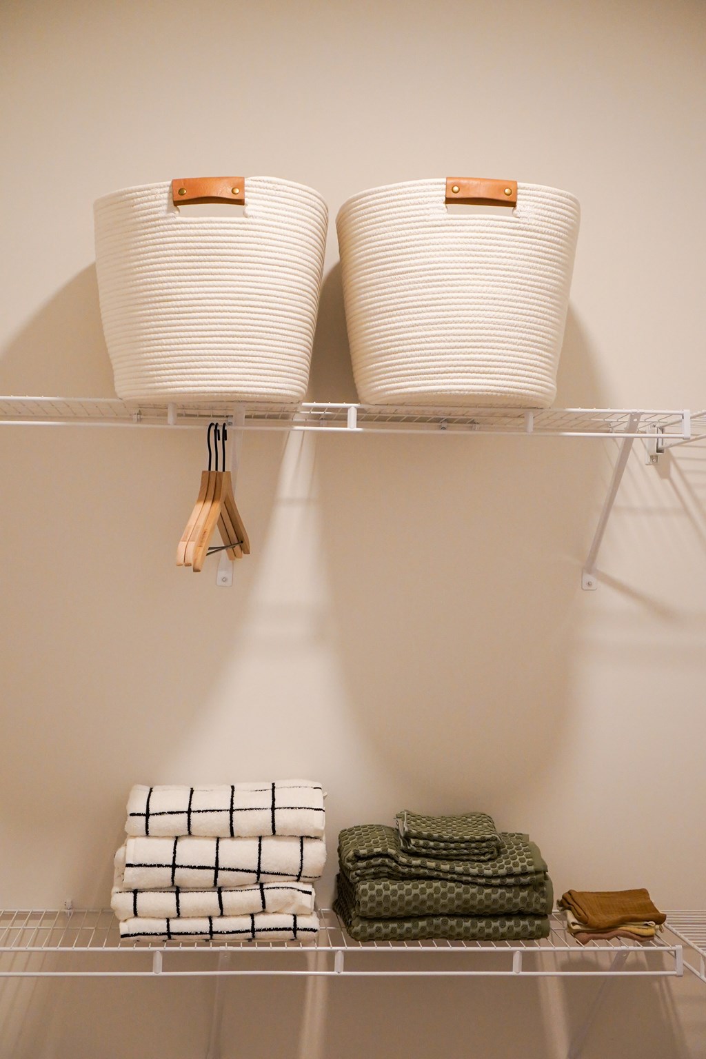 Two white baskets with wooden handles are on a shelf with folded towels.
