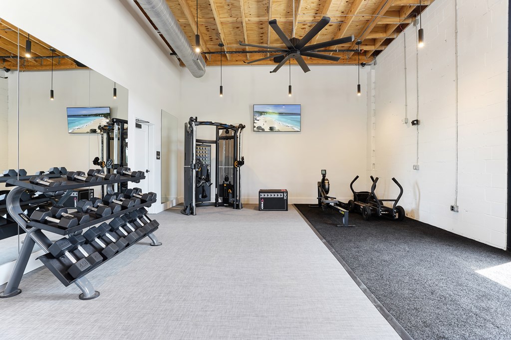 A gym with a variety of equipment including a rowing machine, a treadmill, a weight bench, and a stationary bike.