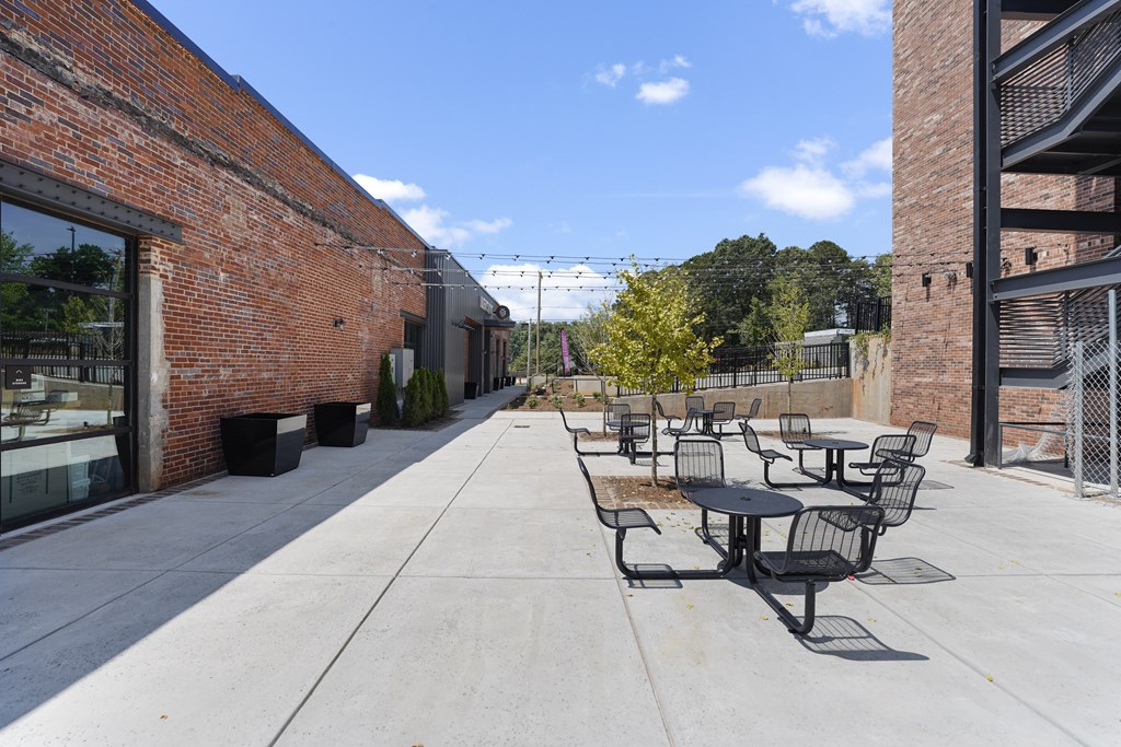 A patio with black chairs and tables is surrounded by brick buildings.