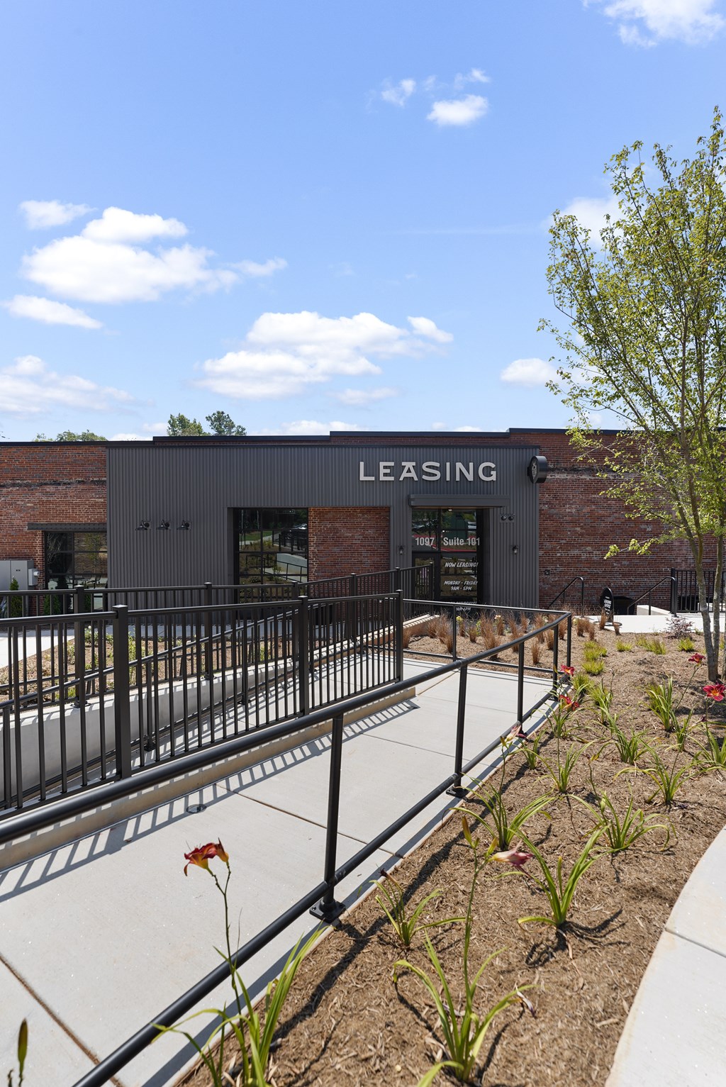 A leasing building with a black fence and plants in front.
