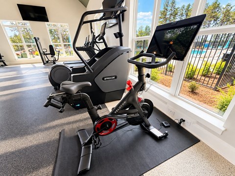 A stationary exercise bike is in a room with a view of a pool and trees outside.