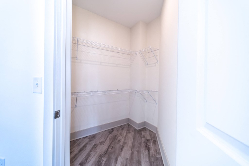 a walk in closet in a bedroom with white walls and a wooden floor