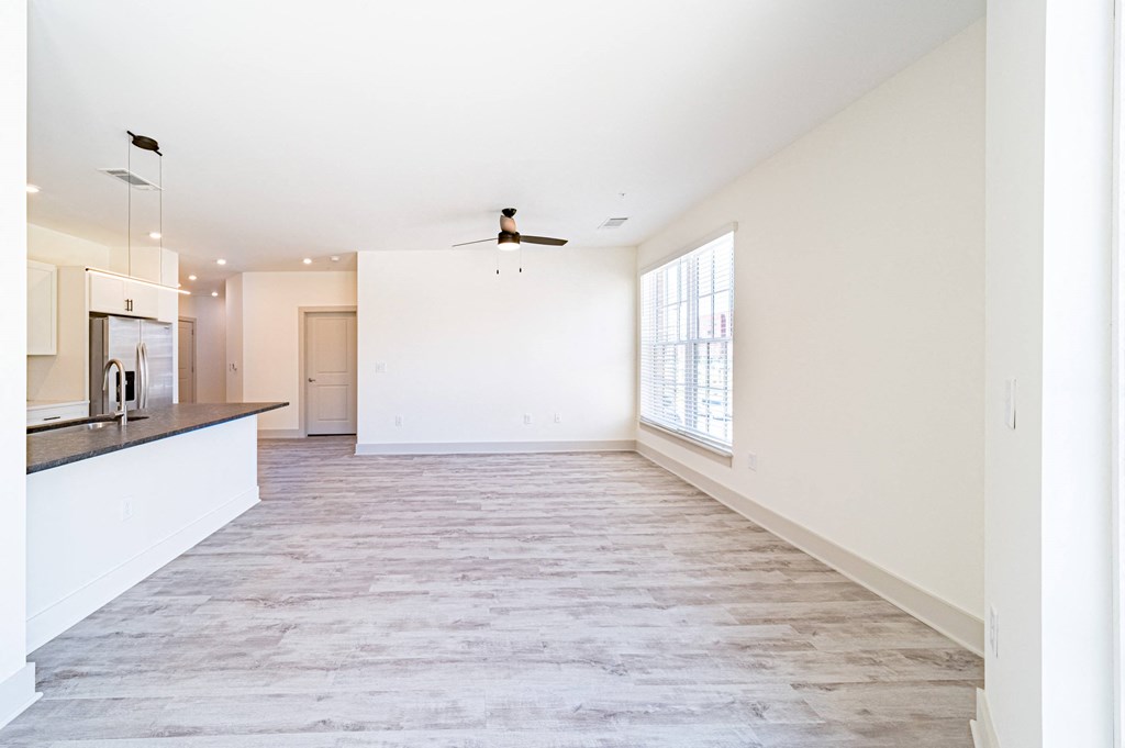 an empty living room with a kitchen in the background