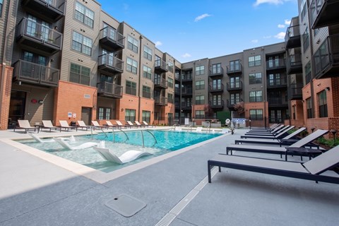 A swimming pool surrounded by lounge chairs and apartment buildings.