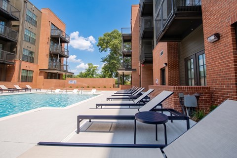 A pool surrounded by lounge chairs and apartment buildings.