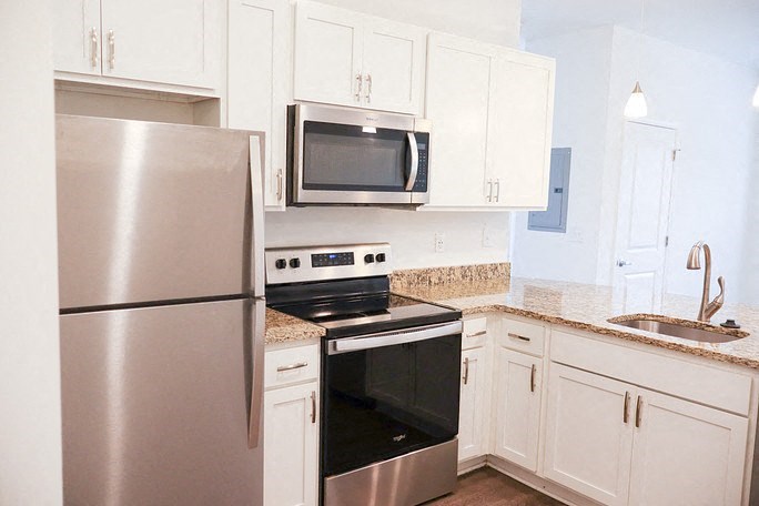 A kitchen with a stainless steel refrigerator, microwave, oven, and cabinets.