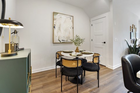 A dining room with a table set for two and a painting on the wall.