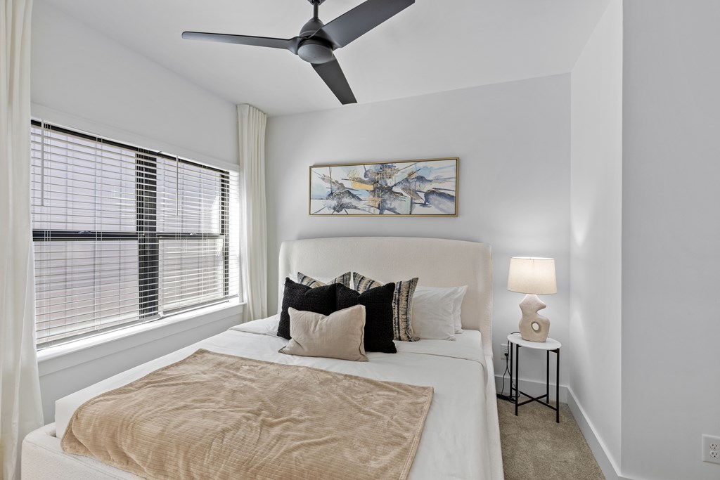 A bedroom with a bed, a ceiling fan, and a painting on the wall.