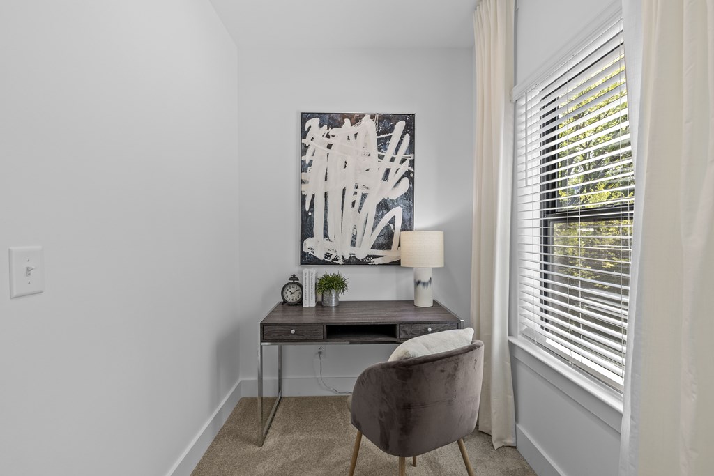 A grey chair sits in front of a desk with a lamp and a clock on it.