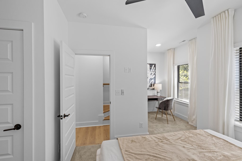 A white bedroom with a bed in the center and a chair in the corner.