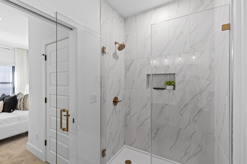 A white bathroom with a marble wall and a glass shower door.