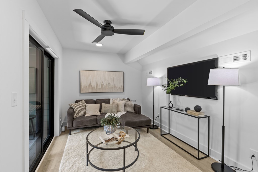 A modern living room with a grey sofa, a coffee table, and a flat screen TV mounted on the wall.
