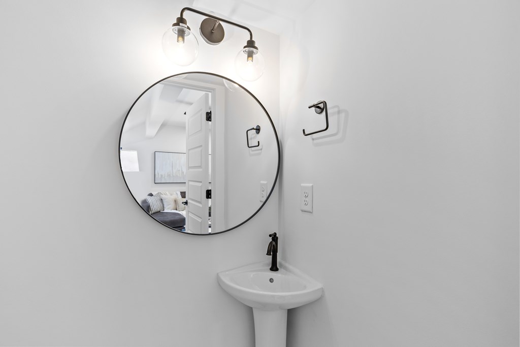 A bathroom with a round mirror, a sink and a light.