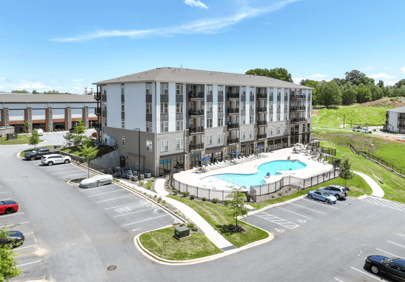 A large apartment complex with a pool in the middle of the parking lot.