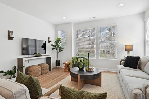 A living room with a white couch, a wooden coffee table, and a flat-screen TV mounted on the wall.