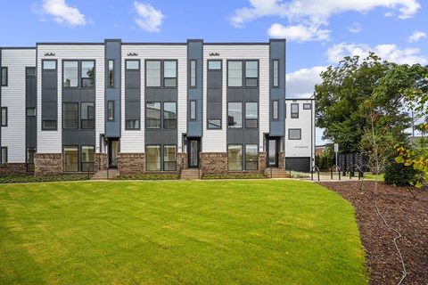 A modern building with grey and white exterior and a green lawn in front.