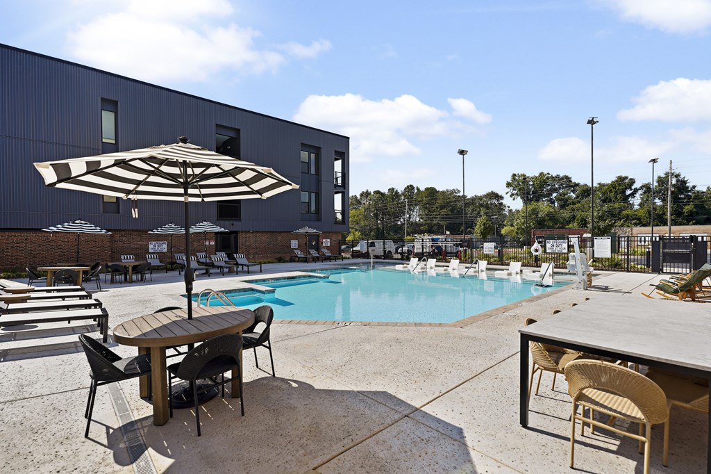 A large umbrella shades a table and chairs by a pool.