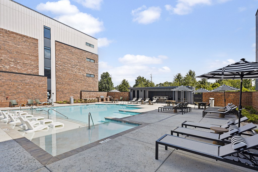 A pool area with sun loungers and a building in the background.