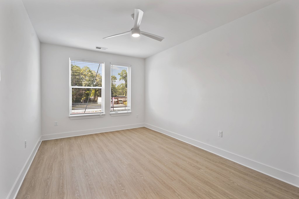 A room with a ceiling fan and a window with a view of a backyard.