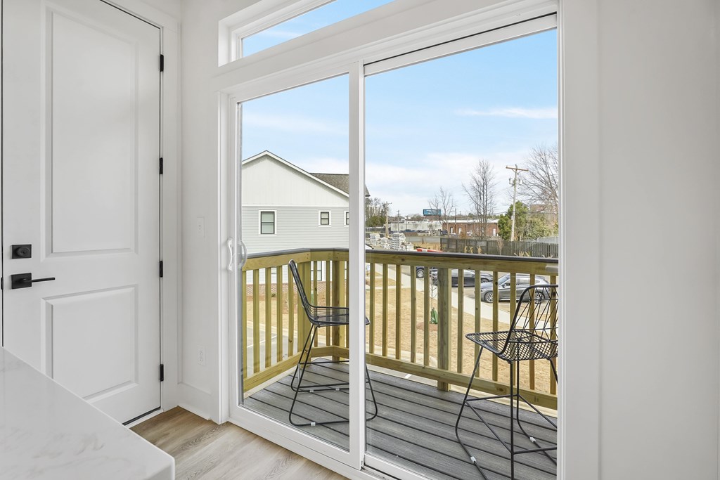 A balcony with a chair and table is visible through a sliding glass door.