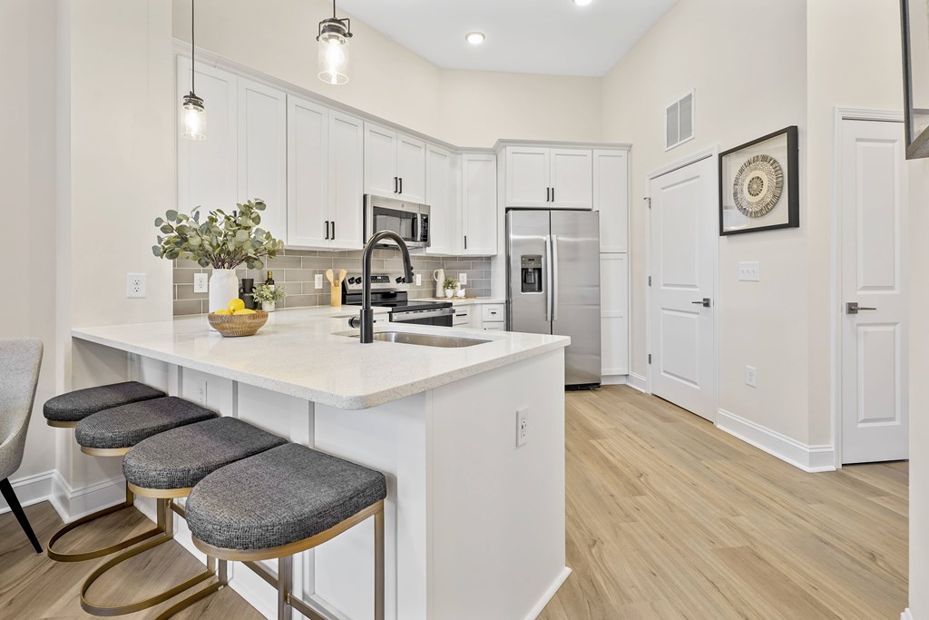 A kitchen with white cabinets and a white island with a vase of flowers on it.