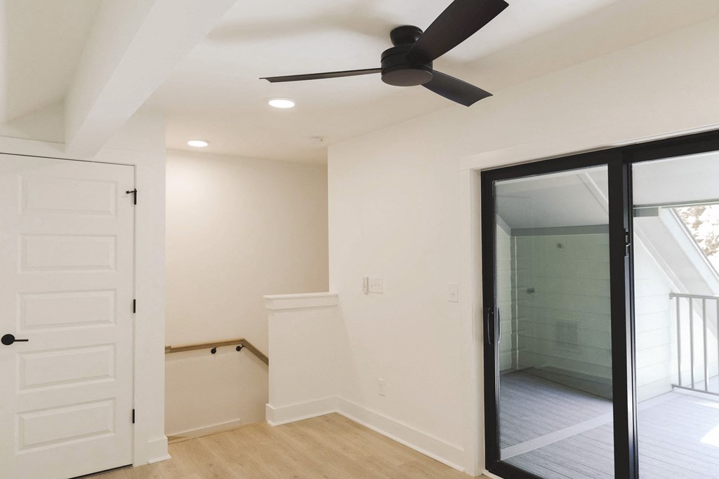 an empty room with a ceiling fan and a glass door to a bathroom