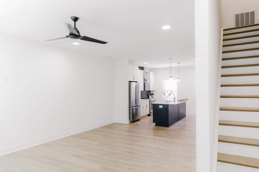 a living room with white walls and a kitchen with a staircase