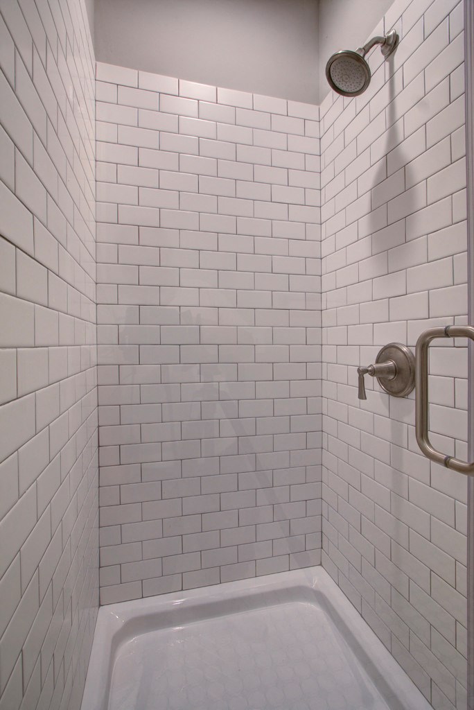 A white tiled shower with a shower head and a faucet.