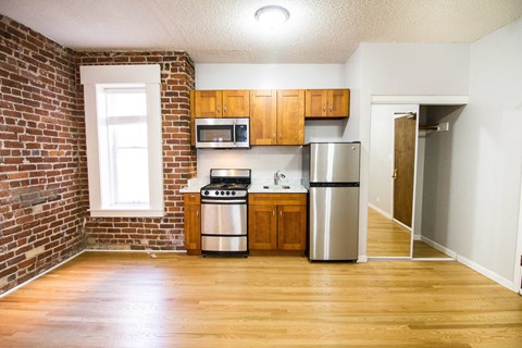 a small kitchen with a brick wall and wooden cabinets and stainless steel appliances