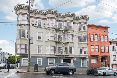 A street view of a multi-story building with a car parked in front.