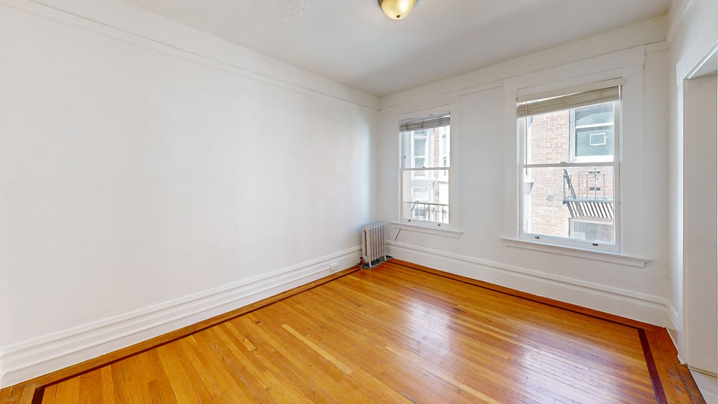 a living room with wood floors and white walls and two windows