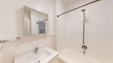 A white bathroom with a sink, mirror, and bathtub.