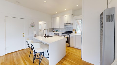 A kitchen with white cabinets and a white island with a chair.
