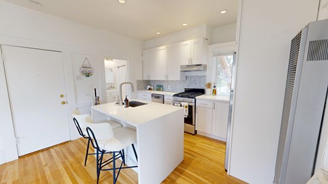A kitchen with white cabinets and a white island with a black chair.