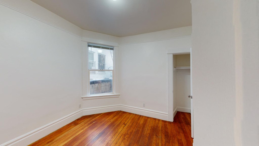 a bedroom with white walls and wood floors and a window