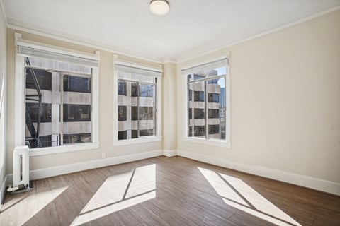 A room with a white wall and a brown floor with a window.