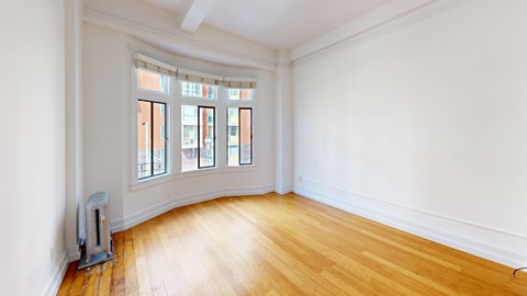 A room with a wood floor and a window with a view of a building outside.