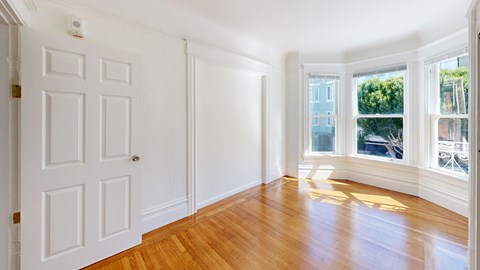 A room with a white door and a window with a view of trees and buildings outside.