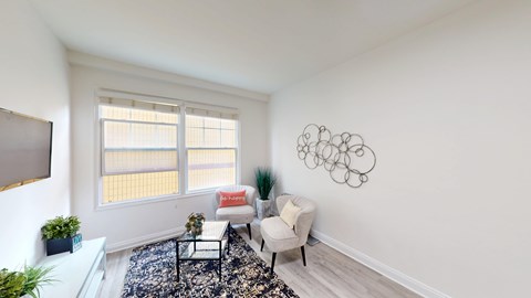 A living room with a white sofa, a black and white rug, a red cushion, a white chair, a potted plant, and a wall art.