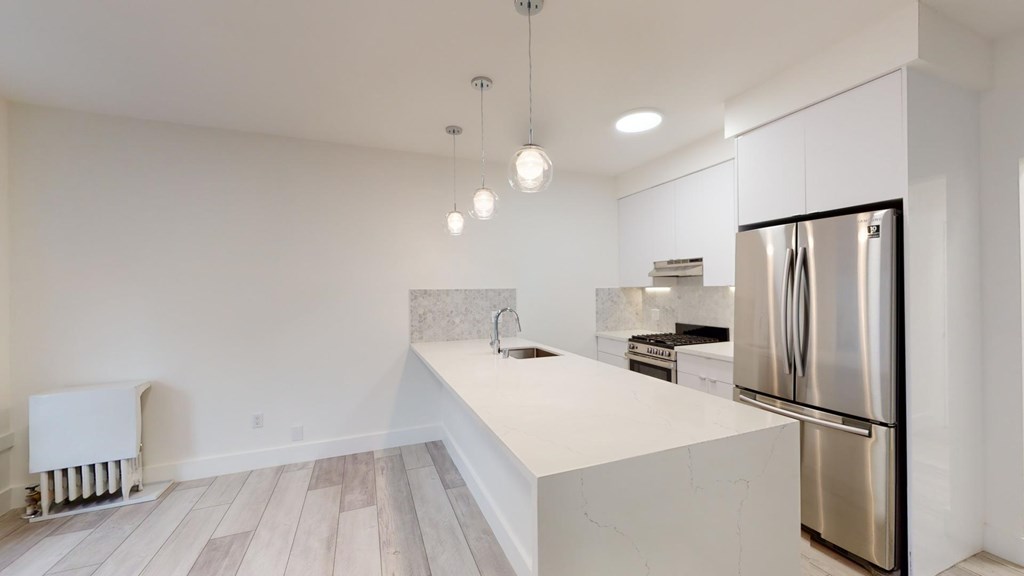 A modern kitchen with a stainless steel refrigerator and wooden flooring.