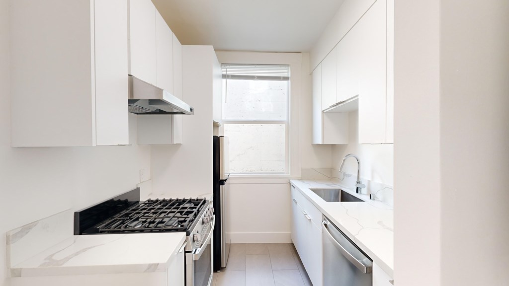 Kitchen with multiple cabinets, refrigerator, stove, range hood, and sink