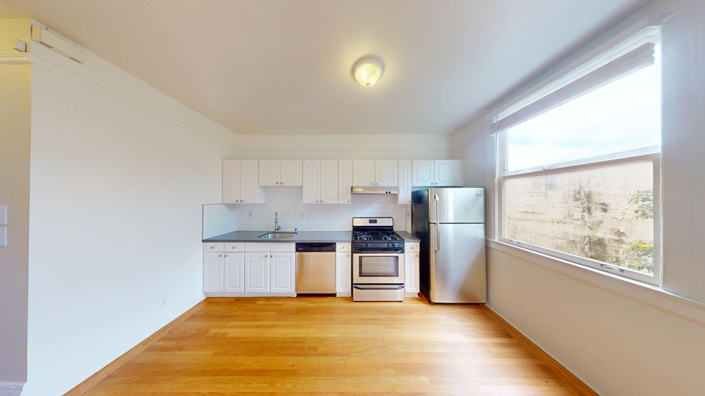 A kitchen with white cabinets and a wooden floor.