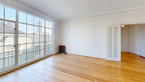 A room with a wooden floor and a large window with a view of a building outside.