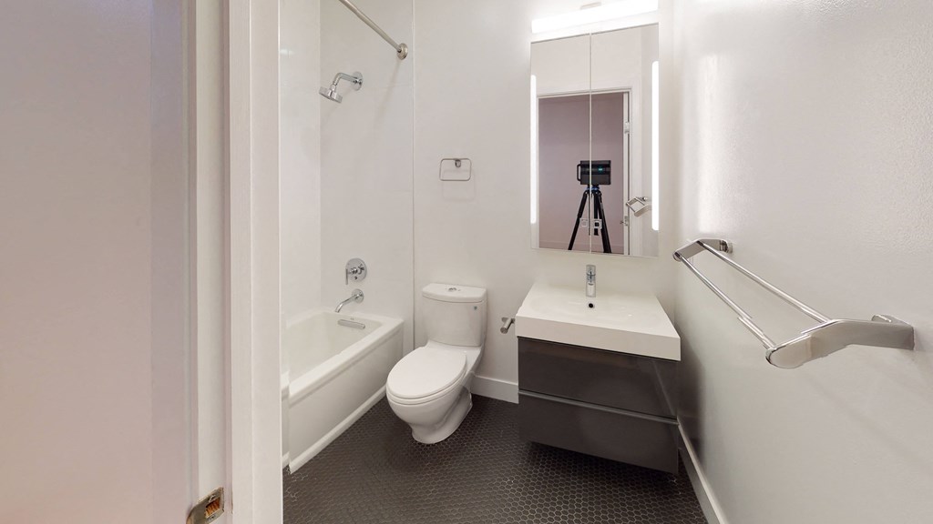 a bathroom with a toilet sink and tub and a camera on a tripod