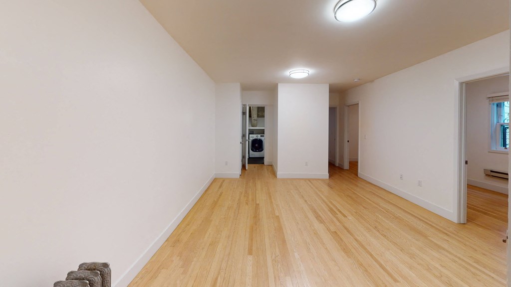a living room with white walls and wooden floors and a laundry room