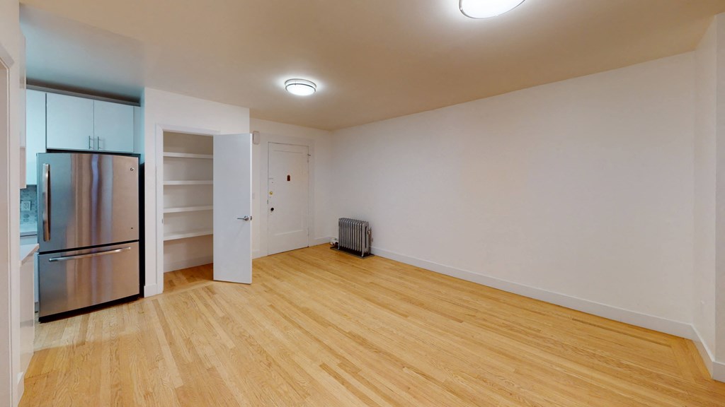 an empty living room with wood flooring and a stainless steel refrigerator
