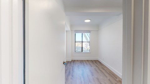 A long, empty hallway with a window and a door at the end.